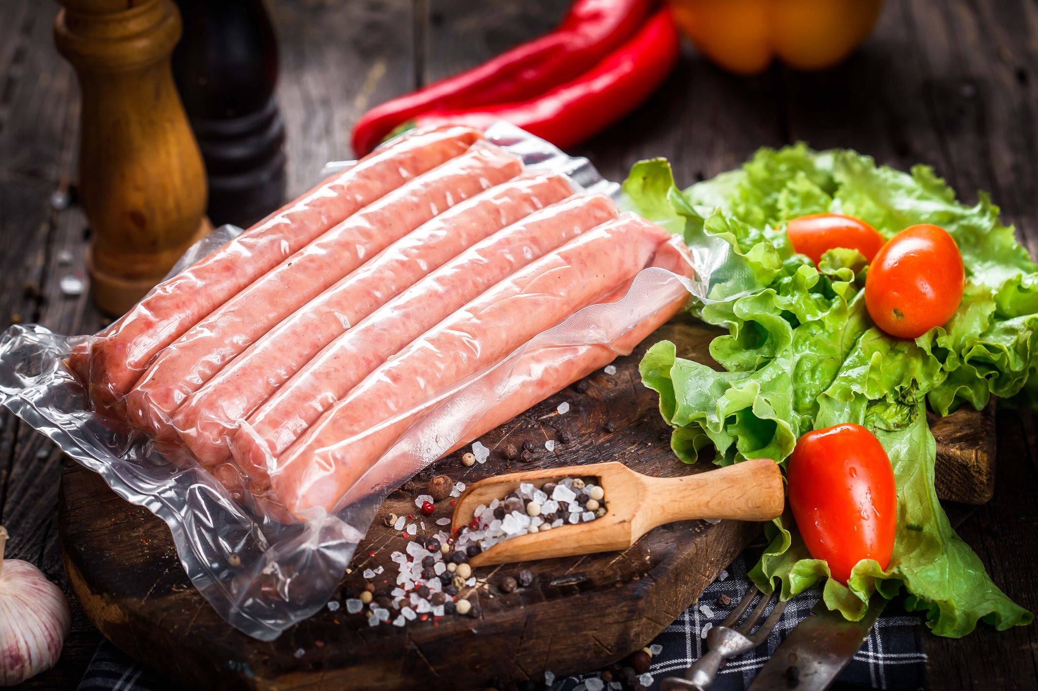 fresh raw sausages, in plastic packaging, on kitchen cutout board with vegetables and herbs, rag cloth, wooden board, table on black isolated background; Shutterstock ID 2077697305; purchase_order: MUDE; job: ; client: Cornelia Geiger; other: ; is_generated: true