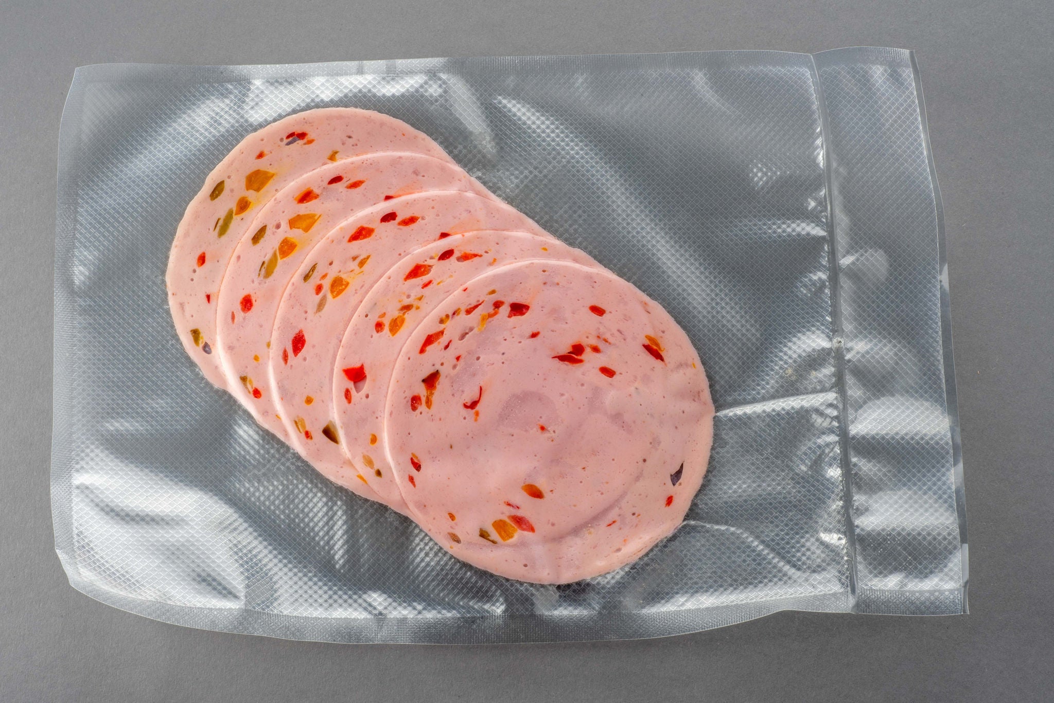 Paprika lyoner sausage slices with bell pepper in vacuum sealed package for sous vide cooking on gray background; Shutterstock ID 2290656959; purchase_order: MUDE; job: ; client: Cornelia Geiger; other: 